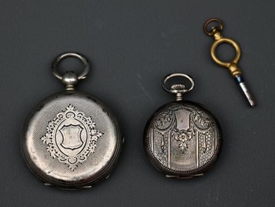 deux montres de poche en argent et une clé posées sur une table