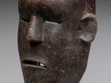 sculpture représentant le visage d'un homme, posée sur un socle, avec un fond gris