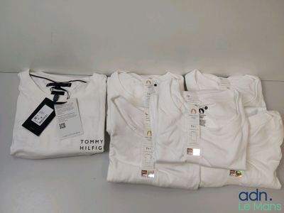 Trois t-shirts blancs sont posés sur une table, à côté d'une paire de ciseaux