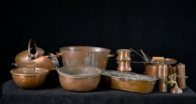 de nombreuses casseroles et poêles en cuivre posées sur une table noire