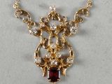 a close up of a gold necklace with a garnett on it