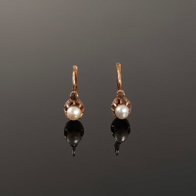 une paire de boucles d'oreilles en perles et en or posées sur une surface réfléchissante
