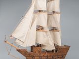 wooden model of a tall sailing ship with white sails on a wooden stand
