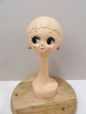 a doll head on a wooden stand on a white surface