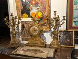 une horloge en or posée sur une table en marbre, devant un tableau