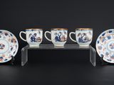 trois tasses et une soucoupe posées sur un présentoir, sur fond noir