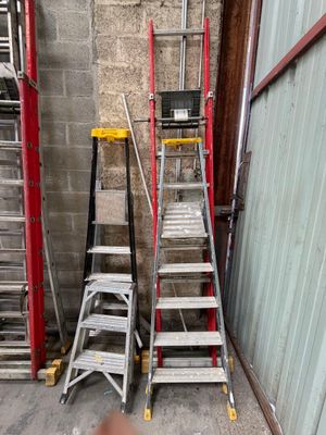 Plusieurs échelles sont alignées contre un mur, à côté d'un immeuble.