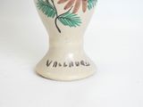 a white vase with a flower on it on a table