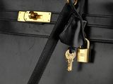 black leather handbag with a gold lock and keys on a black background