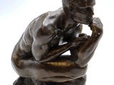 bronze statue of a man sitting on his knees with his hand on his chin