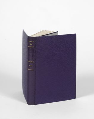 un livre violet posé sur une table blanche, près d'un mur blanc