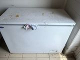 a white refrigerator in a dirty kitchen with a trash can