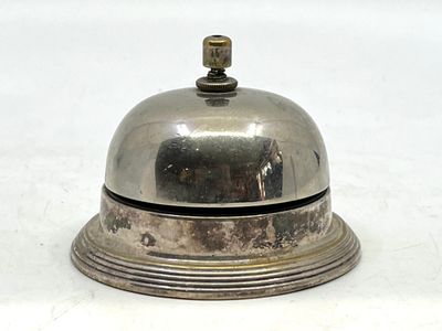 une clochette argentée posée sur une table blanche