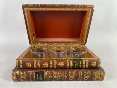quatre verres posés dans une boîte en bois, posée elle-même sur un livre
