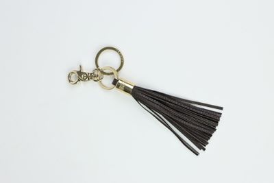 Le porte-clés à pompon en cuir noir est muni d'un anneau métallique plaqué or et d'un pompon en cuir noir