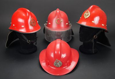 trois casques de pompier rouges sont alignés sur un fond noir