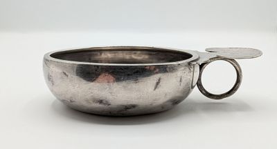 un bol en argent avec une poignée sur une surface blanche