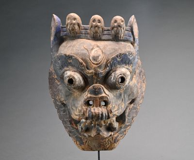un masque orné d'un crâne, posé sur un socle