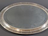 an oval silver tray with a beaded edge sits on a table