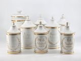 five white and gold canisters sitting on a white surface