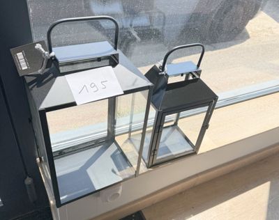 deux lanternes posées sur un rebord de fenêtre sur lequel est accrochée une pancarte