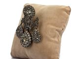 beige pillow with a decorative brooch on it on a white background