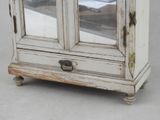 a small white cabinet with a glass door on top of it