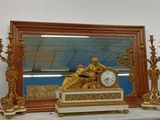 une horloge en or posée sur une cheminée, à côté d'un miroir