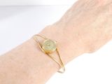 someone is holding a gold bracelet with a green stone on it