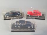 three miniature cars in plastic cases sitting on a white surface