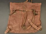 an old brown canvas bag with two straps on a gray surface