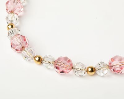 a close up of a pink and gold beaded necklace on a white surface