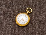 une petite montre de poche en or posée sur un tissu marron