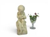 a statue of a boy sitting on a chair next to a vase of flowers