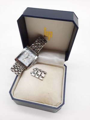 une boîte ouverte contenant une montre, posée sur une surface blanche