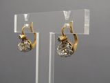 pair of gold and diamond earrings on display on clear acrylic stand