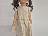 an old doll with a white dress and brown hair on a white surface