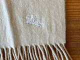 a white blanket with fringes on a wooden table
