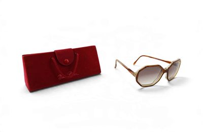 une paire de lunettes de soleil et un étui rouge posés sur une surface blanche, sur fond blanc