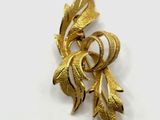 a close up of a gold brooch with leaves on it