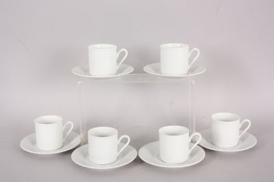 six white cups and saucers are arranged on a clear shelf