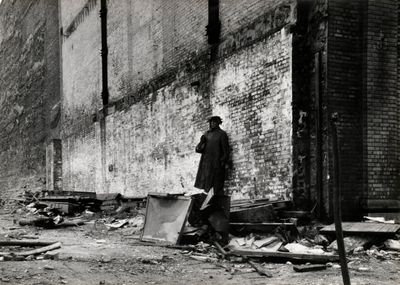 photographie en noir et blanc d'un homme debout devant un bâtiment en briques