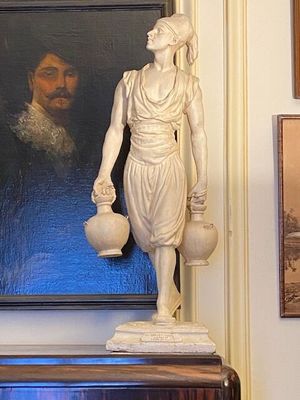 a statue of a woman holding a vase in front of a painting