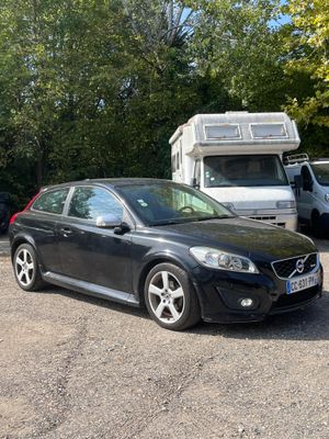 a black volvo car parked in a lot with a camper in the background
