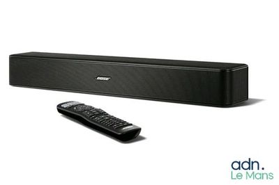 La barre de son est noire et est équipée d'une télécommande placée devant elle.