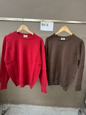 trois pulls suspendus à un portant dans un magasin, avec une étiquette de prix