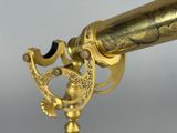 an antique brass telescope on a stand against a gray background