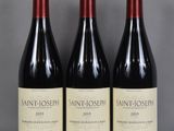 trois bouteilles de vin sont posées sur une table devant un fond gris