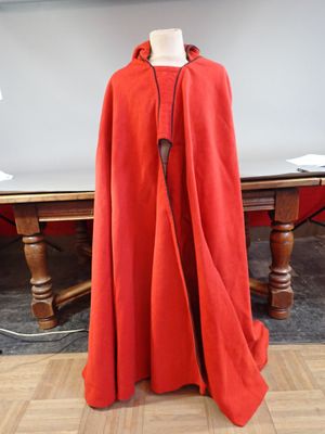 a red cloak on a mannequin in front of a pool table