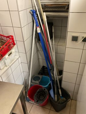 several brooms and buckets are lined up against a wall in a bathroom